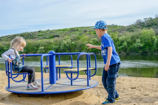 Boy pushing a small girl on a merry-go-round — Stock Photo, Image