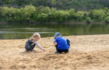 Brother and sister playing on sand near river clipart