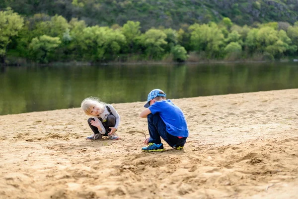 Boy and girl playing on sand near river — Stock Photo, Image