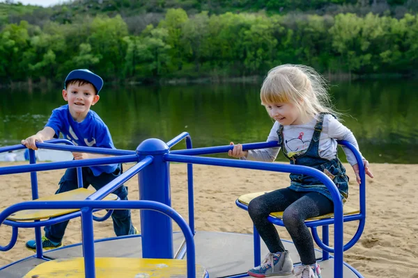 Twee lachende kinderen spelen op een merry-go-round — Stockfoto