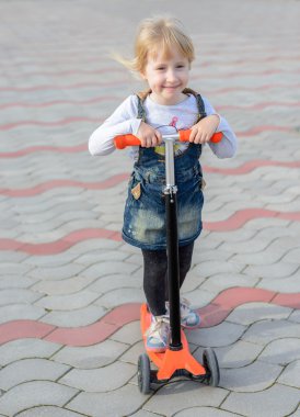 Bir scooter üzerinde poz gülümseyen küçük sarışın kız