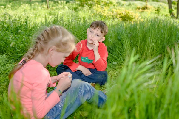 Little boy and girl sitting in long green grass — Stock Photo, Image