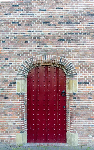 Velha porta cravejado vermelho medieval em uma parede de tijolo — Fotografia de Stock