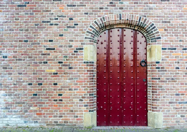 Vecchia porta medievale tempestata di rosso in un muro di mattoni — Foto Stock