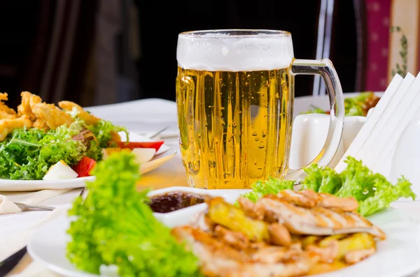 Mok van bier op tafel met vergulde voedsel gerechten — Stockfoto