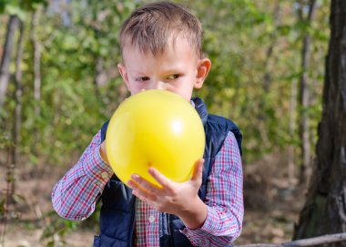 Small boy blowing up a colorful yellow balloon clipart