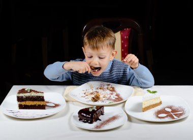 Cute little boy enjoying a treat of party cakes clipart