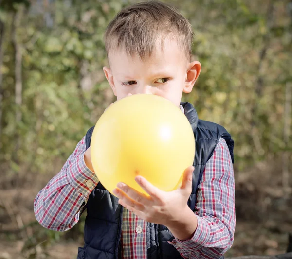 Lilla pojken blåser upp en färgglad gul ballong — Stockfoto