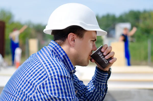 Genç işçi bir inşaat alanı üzerinde kahve yudumlarken — Stok fotoğraf