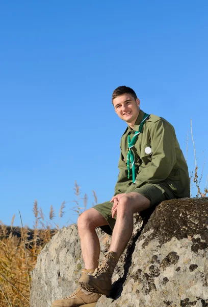 Sorrindo bonito menino escuteiro sentado na rocha — Fotografia de Stock