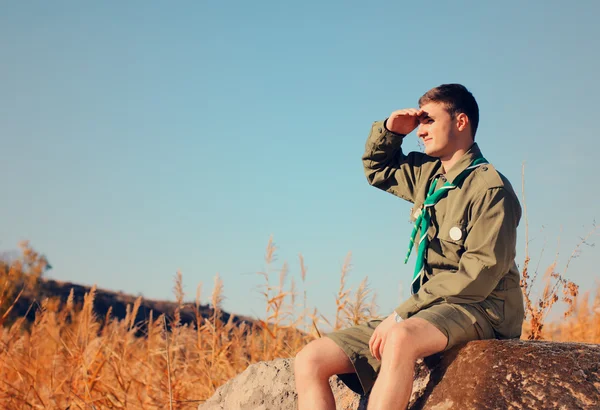 Boy Scout sentado en la roca mirando sobre el campo —  Fotos de Stock