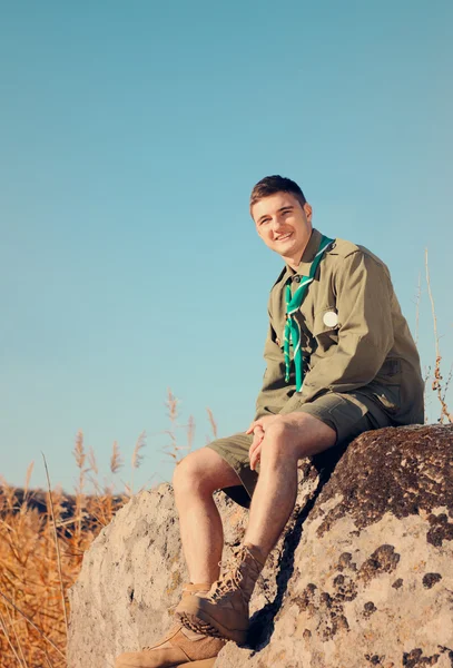 Sorrindo bonito menino escuteiro sentado na rocha — Fotografia de Stock