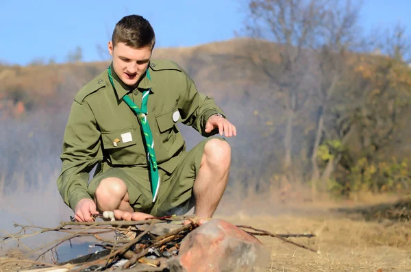 Boy Scout vaření klobás na hůl nad táborák — Stock fotografie