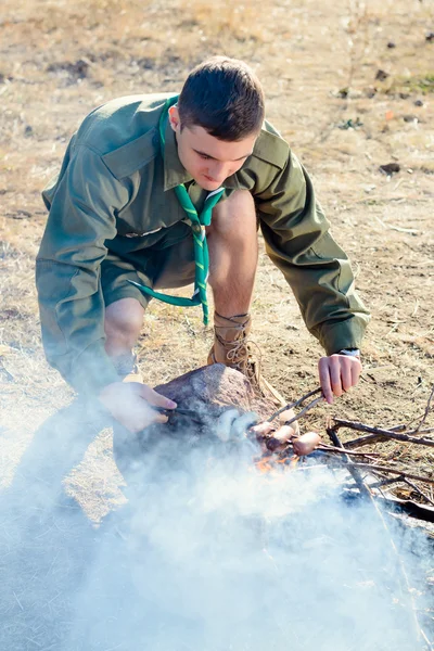 ボーイ スカウト キャンプファイヤーで棒でソーセージを調理 — ストック写真