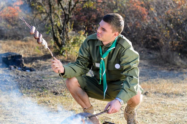 Boy scout cucinare salsicce su bastoni oltre falò — Foto Stock