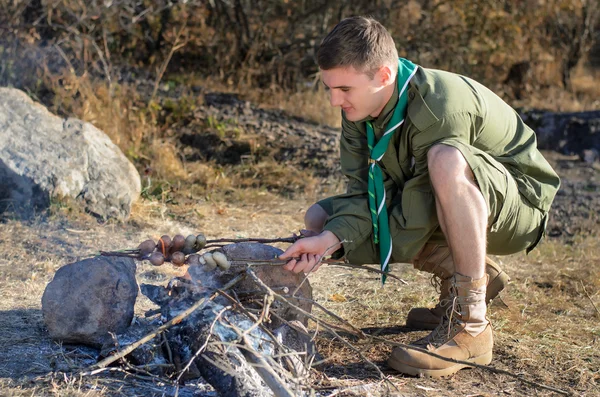 Boy Scout koken worst op stokjes boven kampvuur — Stockfoto