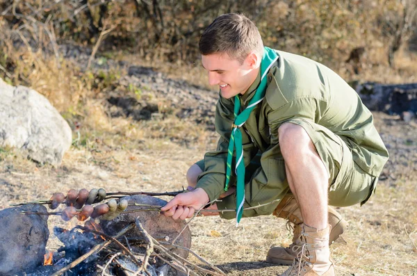 Boy Scout cocinar salchichas en palo sobre fogata — Foto de Stock