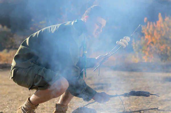 Rapaz escuteiro cozinhando salsichas em paus sobre fogueira — Fotografia de Stock
