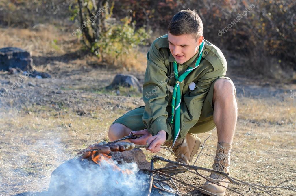 Boy Scout Cooking Sausages on Sticks over Campfire Stock Photo by