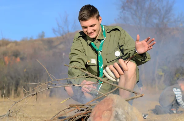 Boy scout cucinare salsicce su bastone oltre falò — Foto Stock