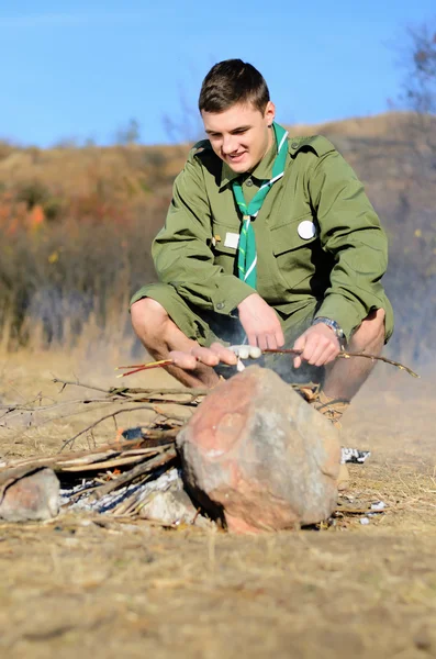 Boy Scout matlagning korv på pinne över lägerelden — Stockfoto
