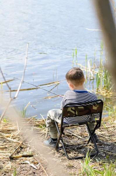 Giovane ragazzo seduto sulla sedia e tenendo asta da pesca — Foto Stock