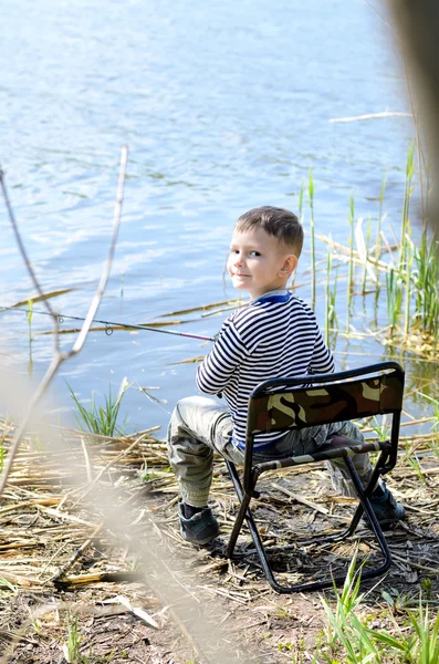 Balık tutma sırasında bir sandalyede oturan gülümseyen genç çocuk — Stok fotoğraf