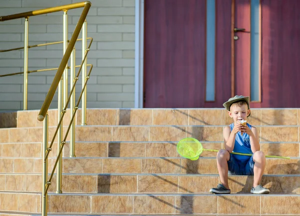 Мальчик с сетью жуков ест мороженое на ступеньках дома — стоковое фото