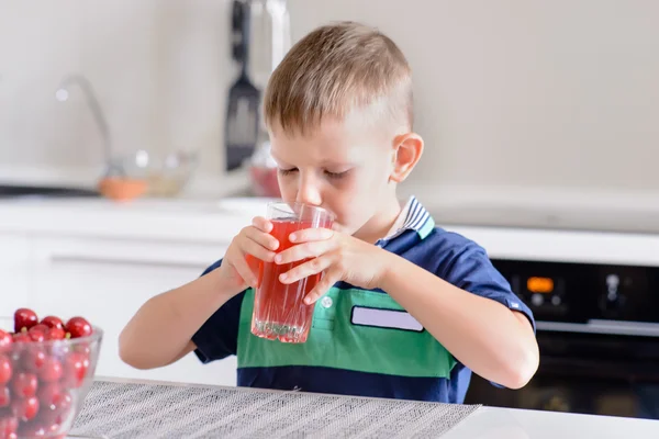 Niño bebiendo jugo de frutas en una cocina — Foto de Stock