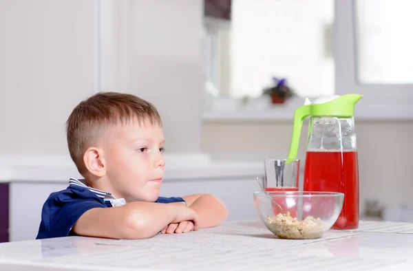 Niño en la mesa de la cocina con tazón de cereales y jugos — Foto de Stock