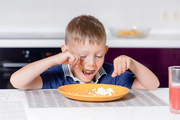 Niño comiendo último bocado de comida en la mesa de la cocina — Foto de Stock