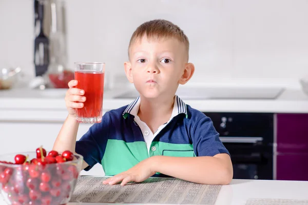 Chlapec v kuchyni stůl pití sklenice červené šťávy — Stock fotografie