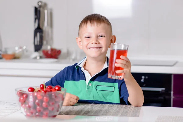 Chico beber vaso de jugo cocina en mesa — Foto de Stock