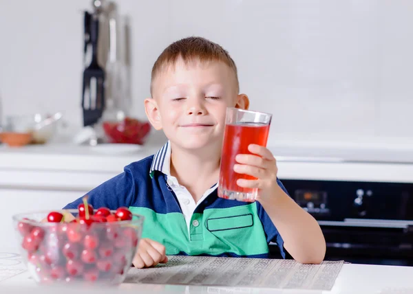 Ragazzo che beve bicchiere di succo di cucina a tavola — Foto Stock