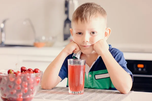 Chłopiec siedzi przy stole w kuchni z szklankę soku — Zdjęcie stockowe