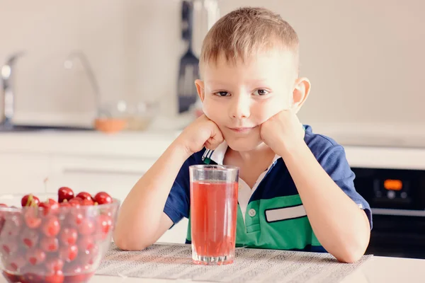 Jongen zit aan de keukentafel met glas sap — Stockfoto