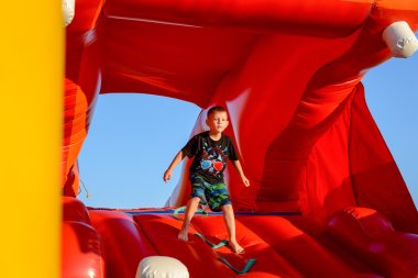 Blond boy playing in red bouncy castle clipart