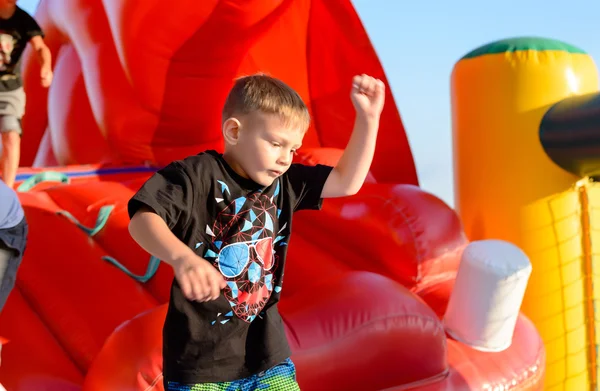 Menino loiro jogando no castelo bouncy vermelho — Fotografia de Stock