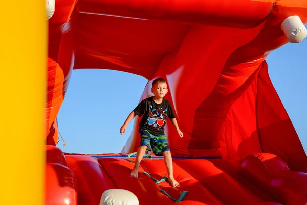 Menino loiro jogando no castelo bouncy vermelho — Fotografia de Stock