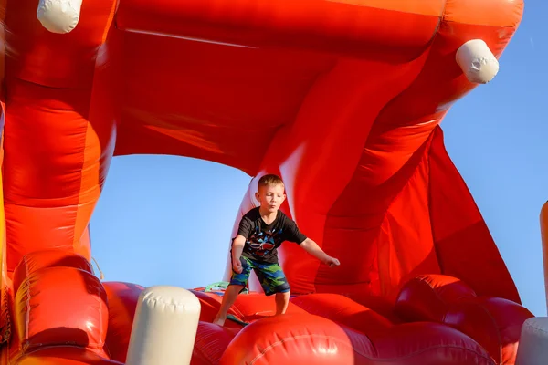 Blond boy playing in red bouncy castle — Stock Photo, Image