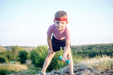 Cute Young Boy Lifting Dumbbell on Top of Boulder