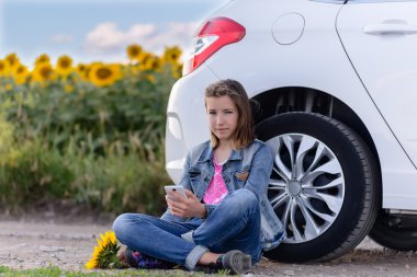 Girl with Phone Sitting on Ground Beside the Car