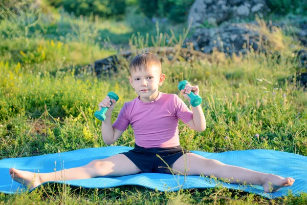 Sonriente niño levantando pesas mientras divide las piernas —  Fotos de Stock