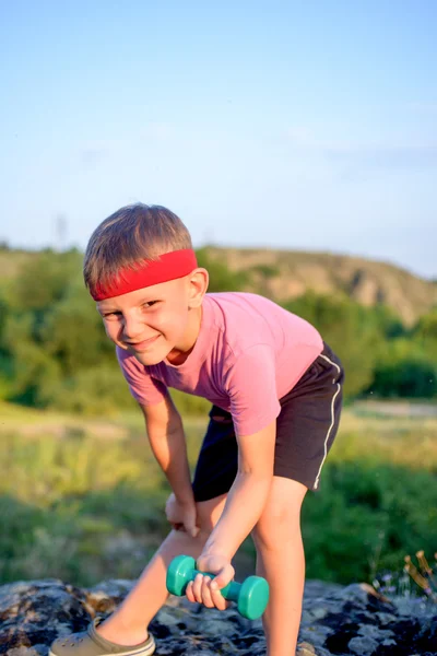 Niedlicher kleiner Junge hebt Hantel auf Felsbrocken — Stockfoto