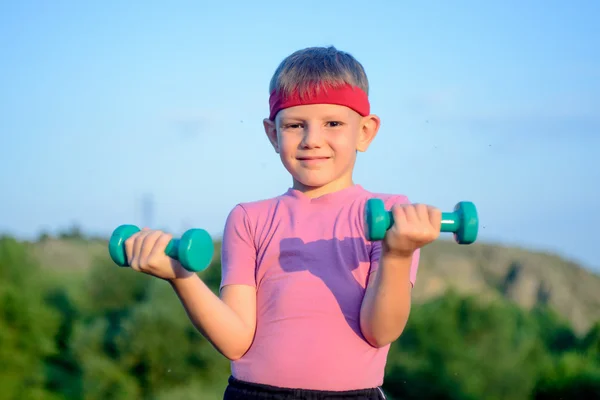 Athletischer süßer Junge, der zwei kleine Hanteln hebt — Stockfoto