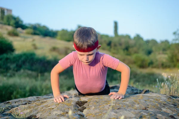 Sportowy młody chłopak robi Push up na górę głaz — Zdjęcie stockowe