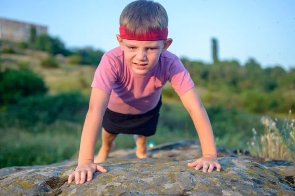Young boy doing push-ups on a rock — Stock Photo, Image