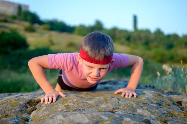 做俯卧撑在一块岩石上的小男孩 — 图库照片
