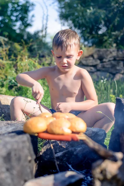 Topless ragazzo grigliate pane e salsicce su bastoni — Foto Stock