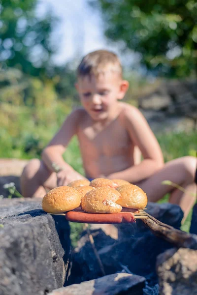 Topless Boy Grilling Bread and Sausages on Sticks — Stock Photo, Image